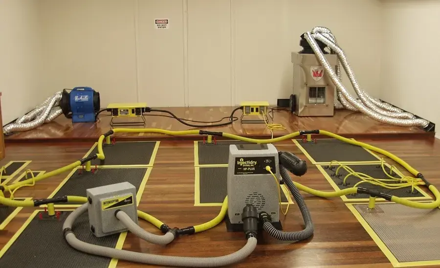 Floor drying mats, hoses and air movers set up on a wet wood floor in a Vacaville home